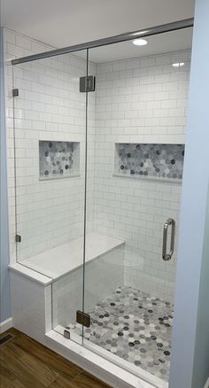 a walk in shower sitting next to a white tiled wall and wooden floored floor