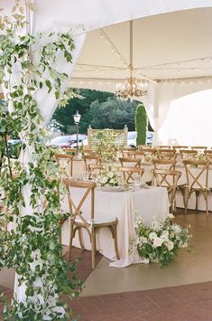 tables and chairs are set up under a tent for an outdoor wedding reception with greenery