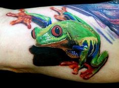 a green frog sitting on the arm of a person with red and blue paint all over it's body