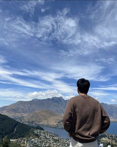 a man standing on top of a lush green hillside next to a lake under a blue sky