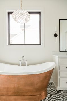 a bath tub sitting under a window next to a white dresser with drawers on it