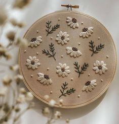 the embroidery is made with white flowers and green leaves on beige fabric, along with small brown pins