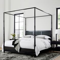 a four poster bed in a white room with a potted plant on the side