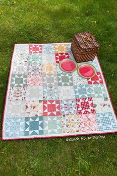 a picnic blanket with plates on it and a basket next to it in the grass