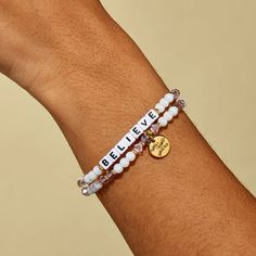 a person wearing a bracelet with the words believe and a gold charm on it's wrist