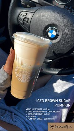 a woman holding a cup of coffee in her hand while sitting in the driver's seat of a car