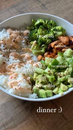 a bowl filled with rice, broccoli and other foods on top of a wooden table