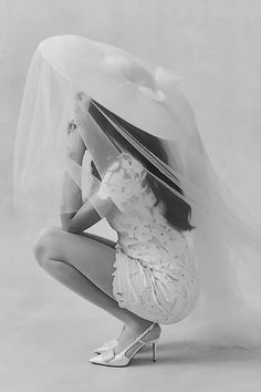 black and white photograph of a woman in wedding dress kneeling down with veil over her head