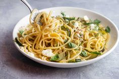 a white bowl filled with pasta and vegetables on top of a table next to a fork