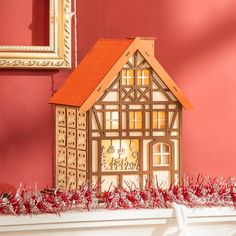 a small model house sitting on top of a mantle next to a framed picture and red wall