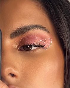 a woman with pink eye makeup holding a cell phone up to her face and looking at the camera