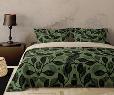 a bed with green leaves on it next to a night stand and table lamp in a room