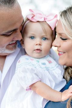 a man and woman holding a baby girl in their arms while she is wearing a pink bow