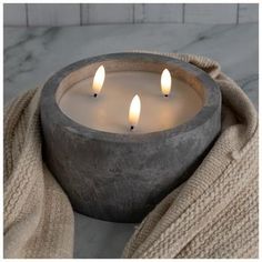 three lit candles in a stone bowl on a marble counter top with a sweater draped around it