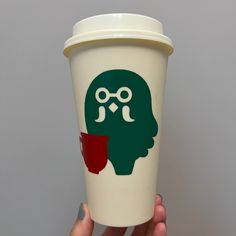 a person holding up a cup with a strange face on the side and a red cup in front of them