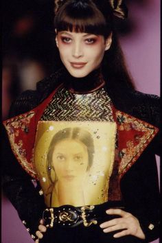 a woman with long black hair holding up a golden piece of art on her chest