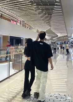 two people are walking through an airport with their back to the camera and one person is on his cell phone