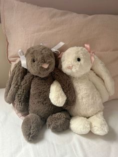 two stuffed animals sitting next to each other on top of a bed with pink and white pillows