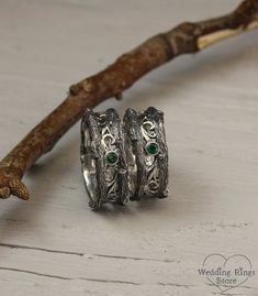 two silver rings with green stones sitting on top of a white table next to a twig