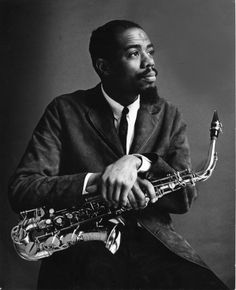 a black and white photo of a man holding a saxophone in his right hand while wearing a suit