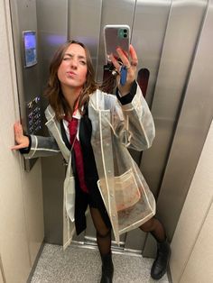 a woman taking a selfie with her cell phone in an elevator stall while wearing a raincoat