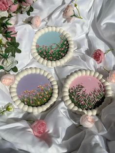 three decorative plates sitting on top of a white cloth covered table next to pink flowers