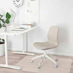 a white desk with a clock on the wall next to it and a plant in a pot