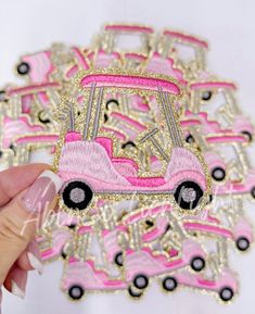 a hand holding a pink and black embroidered patch with a car on the back, in front of a white background