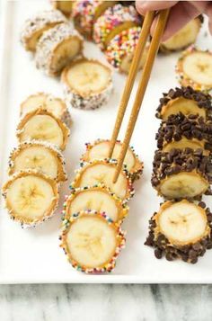 a person holding chopsticks over some food on a white plate with bananas and sprinkles