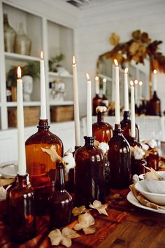 there are many brown bottles on the table with white plates and candles in front of them