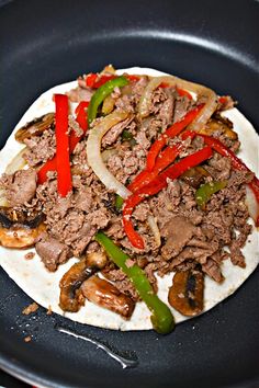 an uncooked tortilla with meat, peppers and onions on it in a skillet