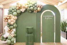 a green and gold balloon arch in front of a wall