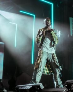 a man standing on top of a stage with his hands in his pockets and lights behind him