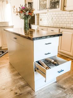 an open drawer in the middle of a kitchen island with white cabinets and wood floors