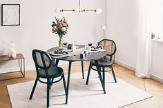 a dining room table with chairs and a vase on top of it in front of a white wall