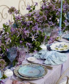 the table is set with purple flowers and plates