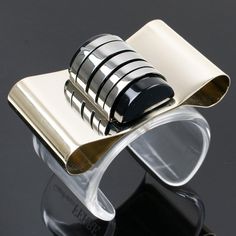 Gianfranco Ferré, Italy, designed this impressive sculptural bracelet bangle. The piece features an oversized cuff shape with Art-Deco-inspired flair. The large clear Lucite band is ornate with a massive bowtie built with pale gold metal and contrasted with gunmetal silvered metal with a black Lucite insert. The bracelet is marked Gianfranco Ferré on the side. Measurements: Inside across is 2.50 in wide (6.3 cm) x 2.07 in deep (5.2 cm) - width is 2.07 in wide (5.2 cm) - the opening is 1.13 in ( Modernist Metal Cuff Bangle, Modernist Bangle Cuff Bracelet For Formal Occasions, Metal Cuff Bracelet, Gianfranco Ferre, Pale Gold, Art Deco Inspired, Bracelet Bangle, Cuff Bracelet, Metallic Silver