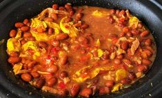 a crock pot filled with beans and other food items in red sauce on top of it