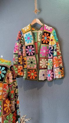 two colorful crocheted jackets hanging on a wall next to a plant and pot holder