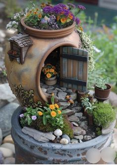 a potted planter filled with flowers and plants next to a small house made out of rocks