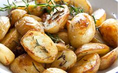 a white bowl filled with potatoes covered in seasoning and sprinkled with rosemary