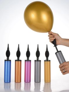 a person is holding a balloon in front of six different colored bottles with black tops