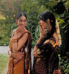 two women standing next to each other with their hands on their mouths and looking at the camera