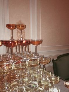 a table topped with lots of wine glasses next to a black chair and white wall