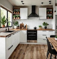 a kitchen with wooden floors and white cabinets, plants on the counter top, and black appliances