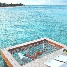 a woman laying in a hammock on top of a wooden dock next to the ocean