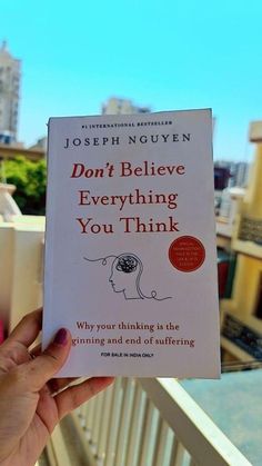 a person holding up a book in front of a balcony with the words don't believe everything you think