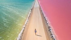 an aerial view of a person walking down a dirt road next to the ocean with pink water