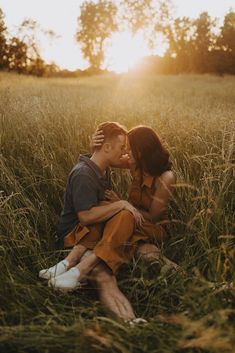 a man and woman sitting in tall grass kissing each other with the sun behind them