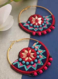 two hoop earrings with beaded details and beads on them, sitting next to a flower